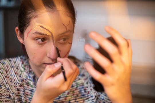 Costumed performer sponging foundation over a scar wax brow with a mirror nearby