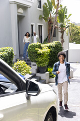 Diverse family watching teenage son in plaid shirt heading to white car on driveway holding phone © wavebreak3