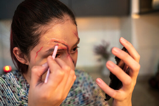 Costumed performer applying a cotton swab to a fresh wound near her eyebrow