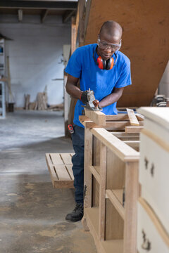 Hand plane smoothing unfinished wooden panel on workbench with scattered sawdust and cabinet frames