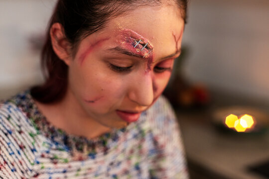 Costumed woman with a gory stapled brow wound looking downward in soft light