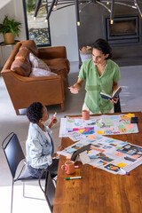 Obraz premium Diverse coworkers collaborating around wooden table in living room with sticky notes, tablet, mugs