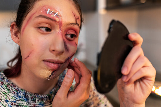 Redhead model retouching a stapled eye wound with a mirror held in her hand