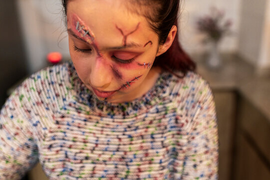 Costumed character inspecting bruised and bloody wounds in a handheld mirror