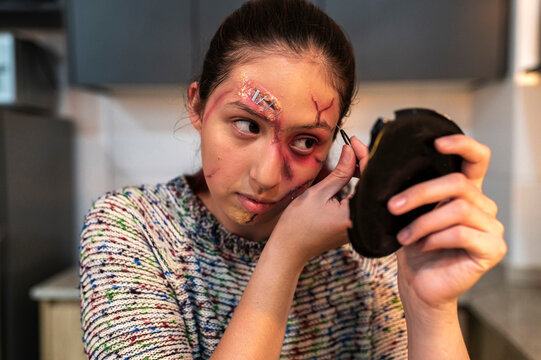 Redhead model holding a phone mirror to review her gruesome facial wounds