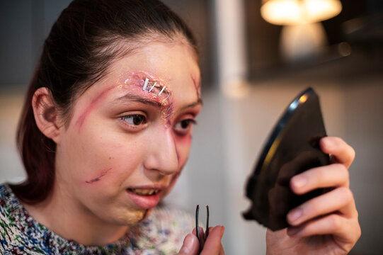 Costumed performer checking her finished facial wounds in a phone screen mirror