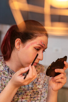 Redhead model brushing mascara onto her lashes with a round mirror in warm light
