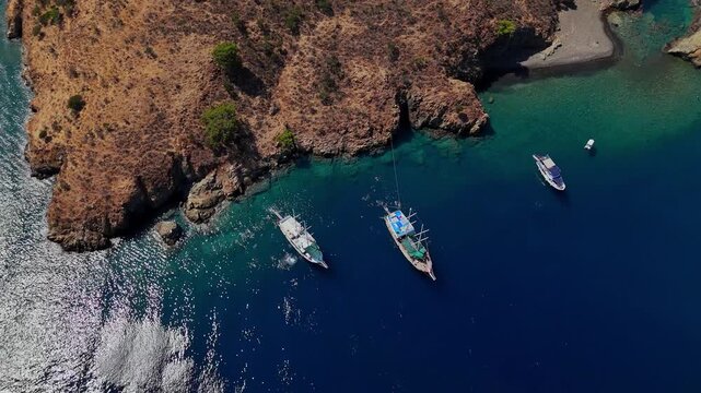 Aerial view of traditional gulet boats anchored near a rocky coastline in clear turquoise water, ideal for summer travel, coastal tourism, sailing, vacation and Mediterranean lifestyle content.