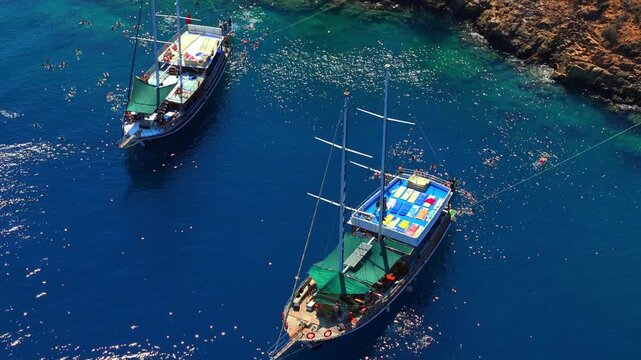 Traditional tour boats anchored in a rocky blue bay with people swimming during a sunny summer cruise, ideal for travel, tourism, coastal vacation and Mediterranean lifestyle content.
