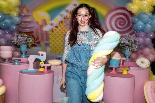 Full body costumed character holding a plush toy in a rainbow candy wonderland