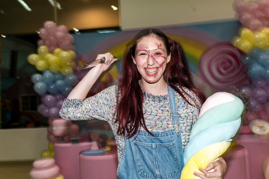 Grinning killer doll character swinging a knife in a pastel candy themed room