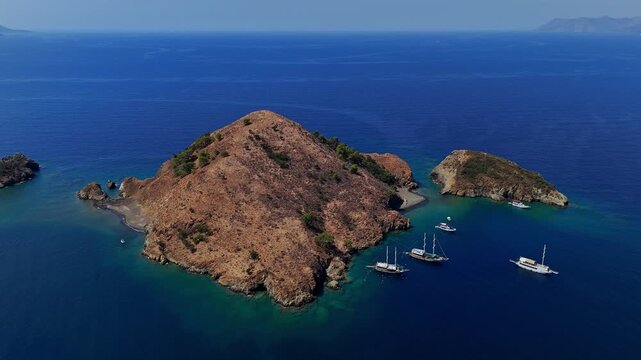 Aerial view of a rocky island surrounded by deep blue sea, turquoise bays and anchored boats, ideal for summer travel, coastal tourism, Mediterranean vacation and scenic nature projects.