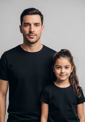 Fototapeta premium Man and daughter in black t-shirt standing together. Father and girl posing for portrait against grey background. Family relationship, love, care and parenthood concept.