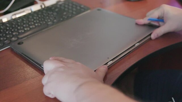 Hands of a craftsman lift and remove the metal back cover of a laptop during disassembly