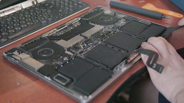 Close-up of a technician's hands disconnecting a black flat cable from a laptop motherboard