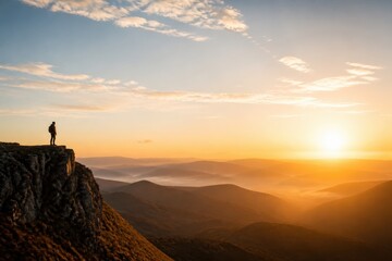 Fototapeta premium Hiker standing on mountain cliff at sunrise overlooking dramatic valley landscape