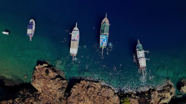 Aerial view of tour boats anchored in clear turquoise water with people swimming near a rocky coast, ideal for summer travel, tourism, vacation, cruise and Mediterranean lifestyle content.