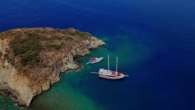 Aerial view of a traditional boat anchored beside a rocky island in clear turquoise water, ideal for summer travel, coastal tourism, vacation, sailing and Mediterranean lifestyle content.
