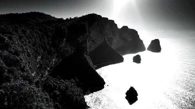 Black and white aerial view of dramatic cliffs and sea stacks along the rugged coastline under sunlight