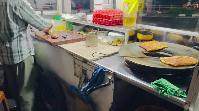 A street vendor selling martabak and terang bulan, typical Indonesian food, is cooking and serving customers at night.

