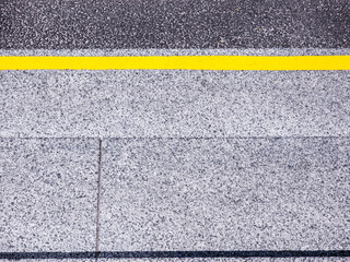 Fototapeta premium Bright yellow strip separating textured dark asphalt from rough gray granite paving slabs, creating a modern abstract patterned background illustrating boundaries and division