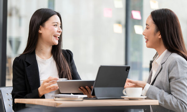 Two happy Asian businesswomen laughing and discussing project in office.