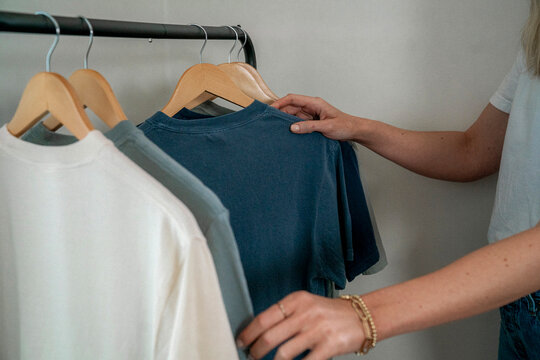 Woman's hand selecting navy t-shirt on clothing rack with gray shirts