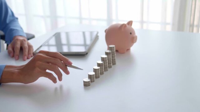 Asian Businessman holding pen counting stacking coin with piggy bank