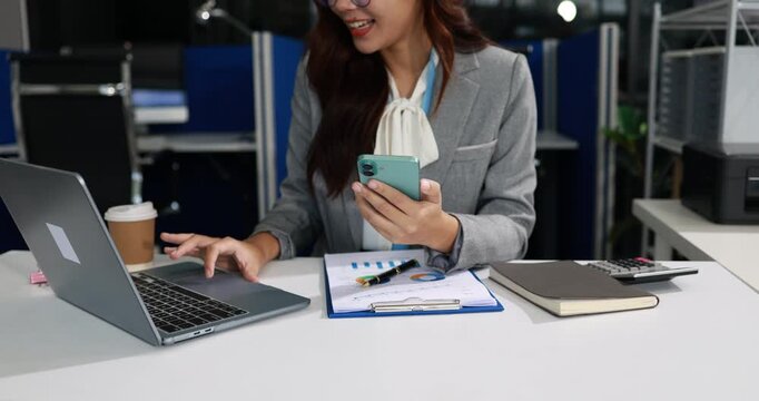 Businesswoman at office desk using laptop and smartphone with coffee, notebook and financial chart, showing multitasking, remote work and modern business planning.