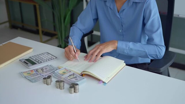 Asian businessman writing on notebook with stacking coin on table money management concept