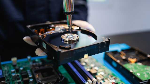 Close-up of a technician repairing a hard drive above a computer motherboard, showing data recovery, hardware service, and modern technology work in a clean lab setting.