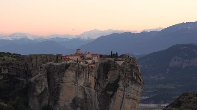 Meteora Greece Monastery of the Holy Trinity (Agia Triada) at Sunset. On Edge of Rocky Cliff. Church 13th century Warm Color with Dramatic Mountains