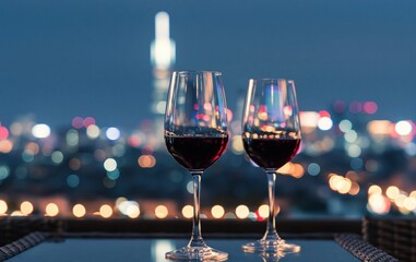 Obraz premium Wine glasses with red wine on balcony table, city skyline bokeh lights evening romance