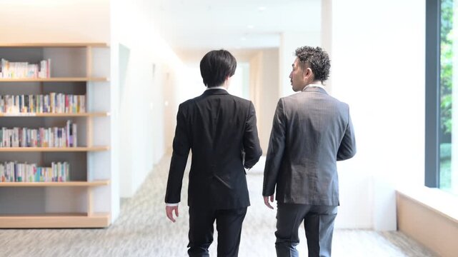 [Slow Motion] Video of a business scene showing a young employee and their supervisor walking and talking&mdash;viewed from behind with their faces obscured