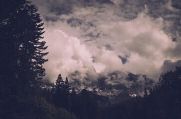 Fototapeta premium Dark clouds and forest silhouettes create a dramatic and mysterious view of the Dachstein Mountains. The cinematic atmosphere makes this image especially appealing for adventure travel, nature story.