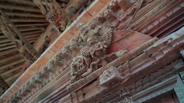 A close-up low-angle static shot showcasing the intricate and weathered ancient wood carvings of mythical deities on a traditional Newar temple structure in Nepal.