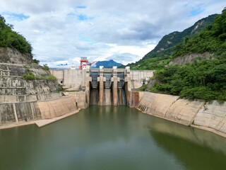 Fototapeta premium Dam on the lake A peaceful mountain river landscape view in nature with green forest trees, water, and clouds in the summer sky