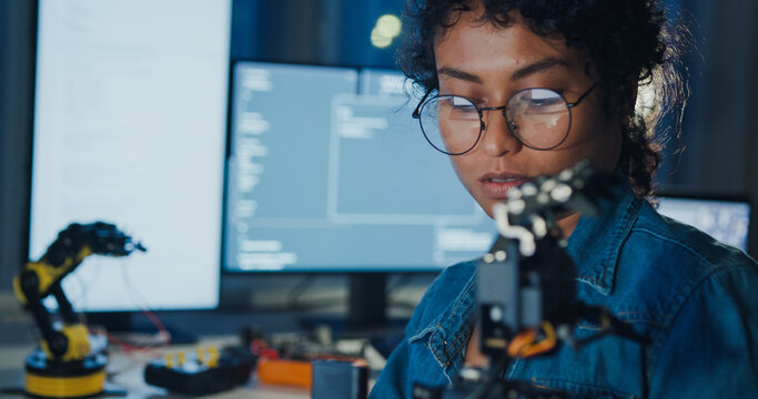 Close-up young Black female programmer coding AI software on multiple screens in night office. Network security, cybersecurity, machine learning, working late, overtime, robotics automation concept.