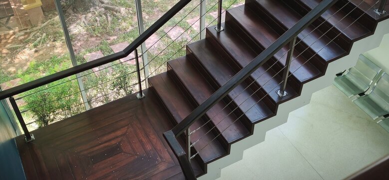 High angle view of modern wooden staircase landing with stainless steel railing and big window.