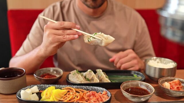 A man holds a traditional Korean steamed dumpling on chopsticks at a Korean restaurant. Asian food. Global food culture