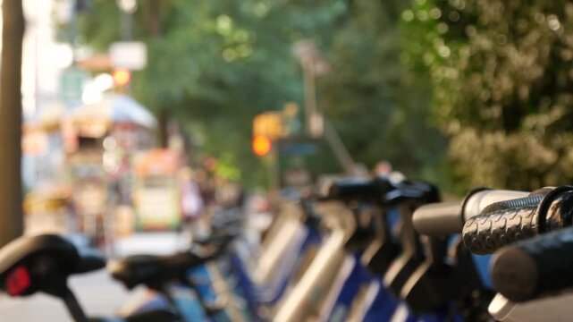 Manhattan Midtown street New York City, United States. Rental bicycle parking on Central Park West, trees summer greenery. Bike for rent in row. Defocused people pedestrian on sidewalk pavement.