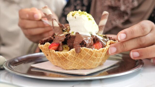 A person eats a waffle bowl sundae likely featuring vanilla ice cream