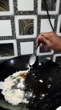 Close up of an Asian man frying crunchy traditional Indonesian cracker batter called rempeyek or peyek with tiny shrimp (udang kecepe) in a black wok with hot boiling oil.