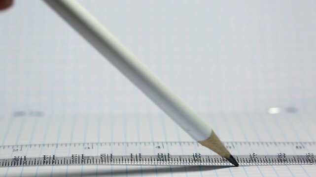 A student draws with a pencil on a ruler in a notebook, drawing