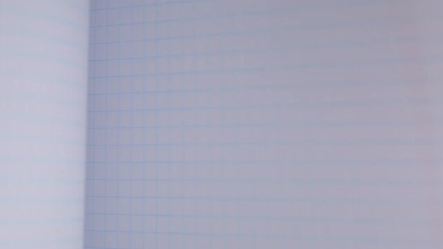 Flipping through the pages of a squared notebook, close-up view of the notebook paper background