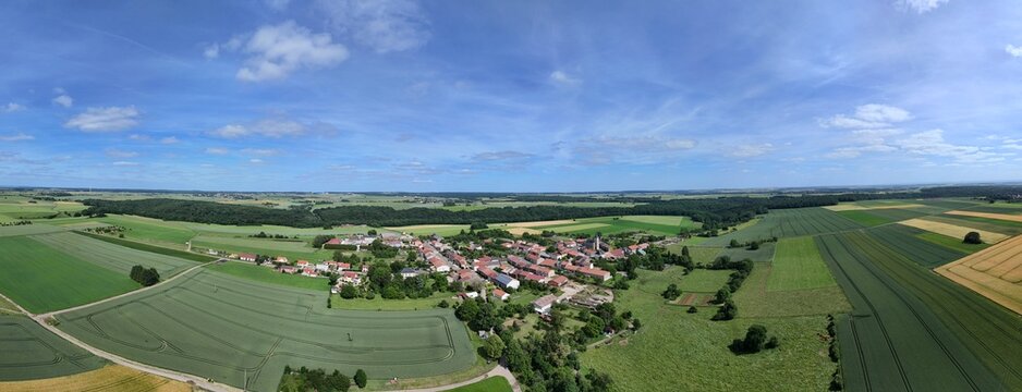 Vue a&eacute;rienne panoramique du village de Laix, en Meurthe-et-Moselle, Lorraine. La commune rurale avec ses habitations et ses b&acirc;timents entour&eacute;e de champs et de cultures. Ciel bleu et nuages