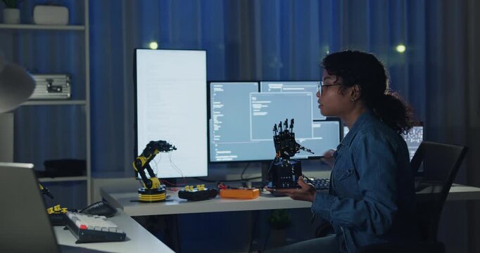 Young African American female programmer coding AI software on multiple screens in night office. Network security, cybersecurity, machine learning, working late, overtime, robotics automation concept.