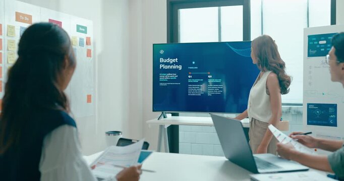 Group of Asian businesspeople work together leads business meeting uses presentation TV with revenue, profit or sale statistics in office. Financial generation z team brainstorm on e-Commerce project.