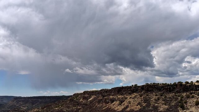 A sweeping drone timelapse capturing a powerful monsoon storm rolling over a rugged southwest canyon ridge. Atmospheric dark clouds build as rain shafts sweep across the majestic desert plateau.