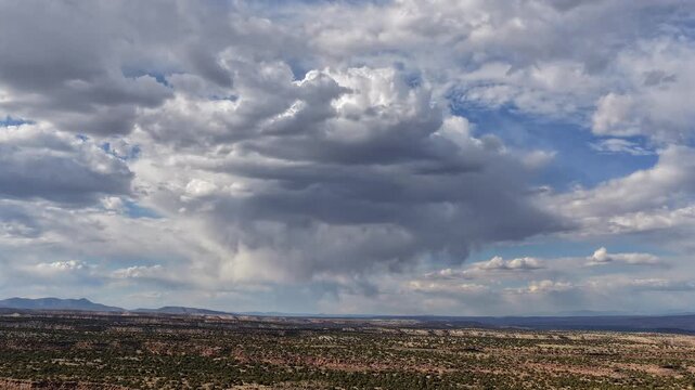 Steady aerial timelapse of a dynamic raincloud morphing over vast desert mesas. Shifting shadows and localized rain showers evolve beautifully across the rugged southwest landscape.